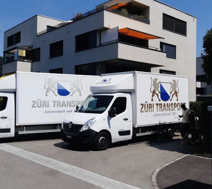 Zwei Umzugswagen von Züri Transport vor einem Mehrfamilienhaus